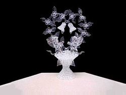 Angels wedding cake top with a solid glass heart, wedding bells and lots of flowers and leaves on a knitted glass base.