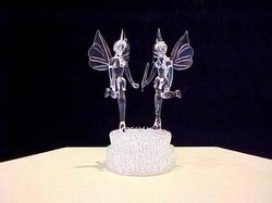 fairies wedding cake top. It has 2 solid glass fairies with wings holding hands on a knitted glass base.