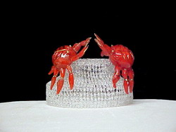 2 solid glass crabs reaching for each other standing on a knitted glass base wedding cake top